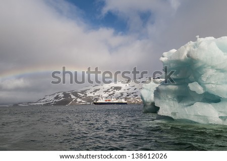 Cruise ship under a rainbow cruising past an iceberg in Hornsund Svalbard Norway within the arctic circle.