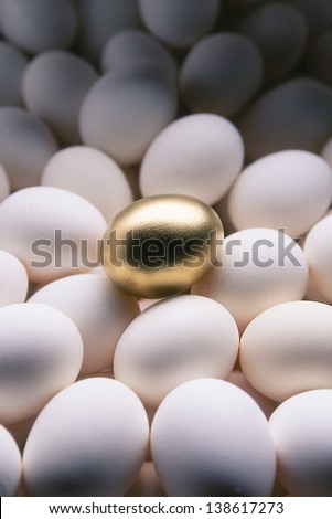 Still life of a golden egg sitting on a field of white eggs.