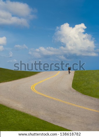 Young woman with raised arms happily hiking up hill along a curving paved path.