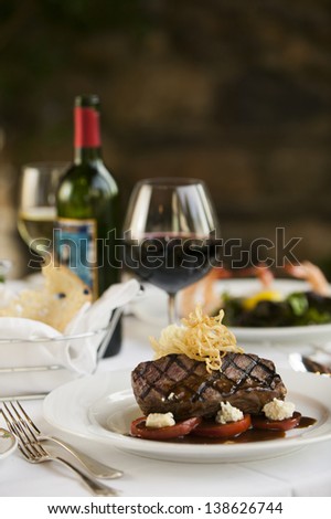 A fillet mignon steak dinner with a bottle and glass of red wine in a fine restaurant setting.