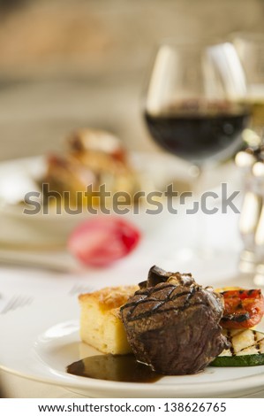 A fillet mignon steak dinner with a glass of red wine and a tulip in a fine restaurant setting.