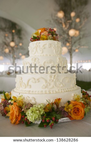 Fancy wedding cake with flowers inside a large event tent.