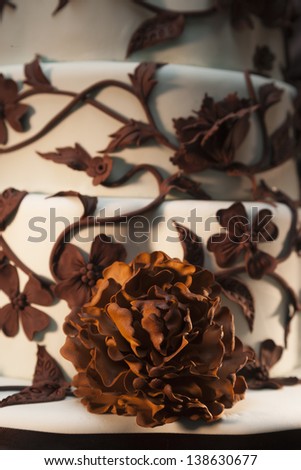 Close-up of a white wedding cake with chocolate flowers, petals and vines.