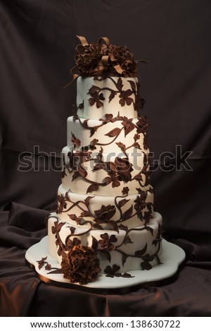 Still life of a white wedding cake with chocolate flowers, petals and vines.