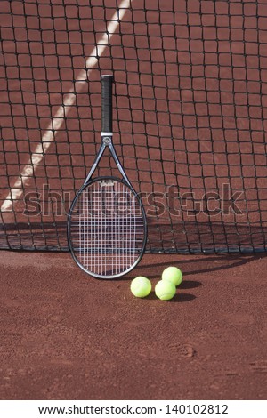 Still life of tennis balls and a racket on a red clay tennis court.