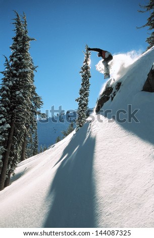 Snowboarding off a cliff off piste on a sunny day in Donner Pass, California, USA