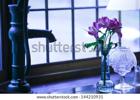 Still life of an old fashioned hand water pump and pink flowers in a tall vase.