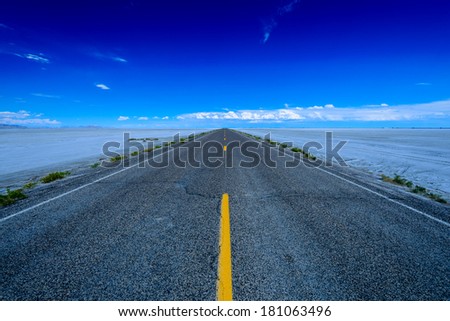Long road disappearing into the horizon surrounded by the salt flats in Wendover, Utah, USA