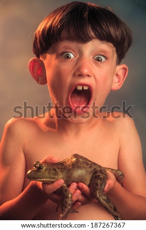 Excited young boy holding a live large frog.