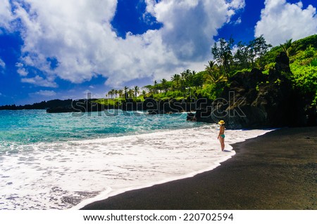 Woman standing in the waves on a black sand beach on the Road to Hana, Maui, Hawaii, USA