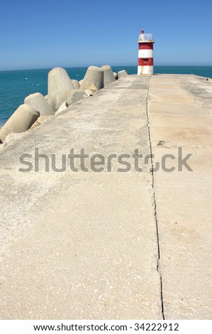 small red lighthouse at the end of a concrete pier