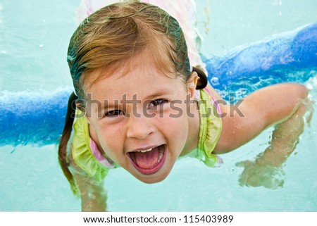 Cheerful girl playing in a swimming pool with a foam float