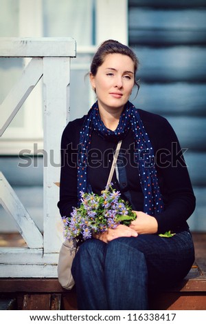 beautiful young woman sitting on the steps outside the house with a bouquet of wild flowers