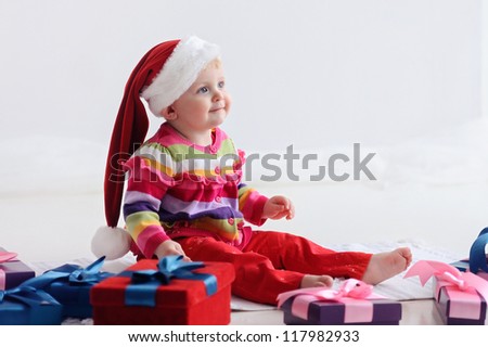 Happy baby sitting on the floor near boxes with gifts. Girl in santa hat. Christmas.