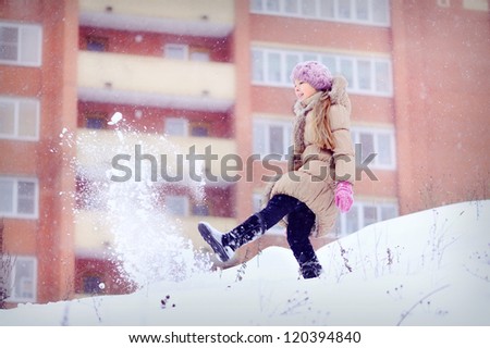 Girl on a high mountain. Lots of snow and cold. Portrait of a child in the winter. Throws snow foot. In the background, a large house.