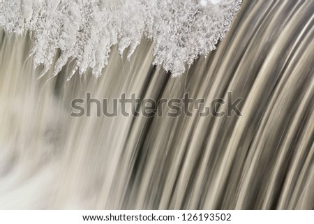 Landscape, of the Battle Creek River Cascade captured with motion blur and framed by icicles, Michigan, USA