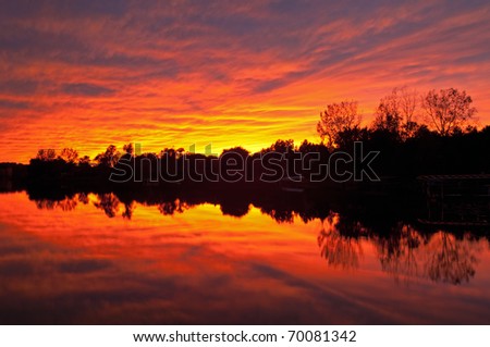 Brilliant red sunset and shoreline of Lake Doster with reflections in calm water, Michigan, USA