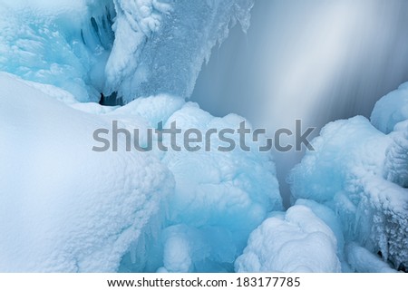 Winter landscape of cascade captured with motion blur and framed by blue ice, Gull Creek, Michigan, USA