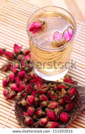 Dried roses, wooden scoop and a glass of rose tea on bamboo mat