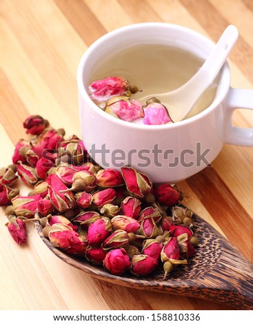 Dried roses, wooden scoop and a cup of rose tea on simple background