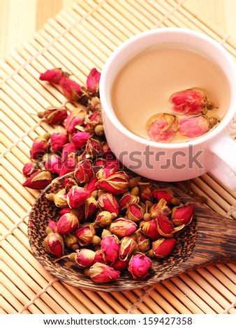Dried roses, wooden scoop and a cup of rose tea on bamboo mat