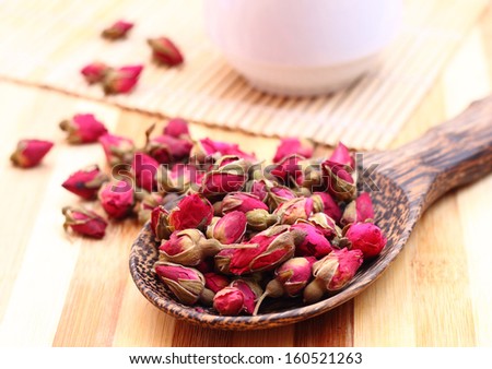 Dried roses, wooden scoop and a cup of rose tea on bamboo mat