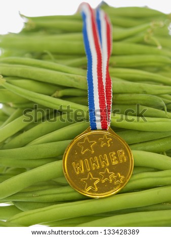 green beans with a gold medal winner pendant on a wooden background