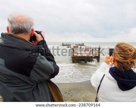 A women and a man taking a picture of something taking place on a bridge.