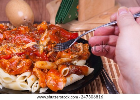 Cooked pasta (penne) with red sauce and vegetables served on a black plate.