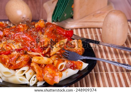 Cooked pasta (penne) with red sauce and vegetables served on a black plate.