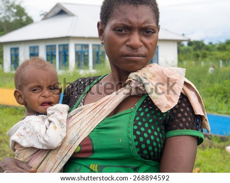 Dekai, Indonesia - January 13, 2015: Tired woman holding on her shoulder a small child, wrapped in a shawl.