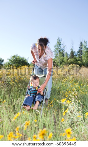 Mother pushing her baby son in a stroller offering him a flower to play with