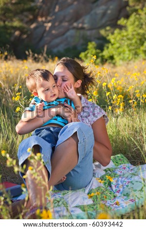 Mother kissing her son, sitting on a blanket in middle of wildflowers