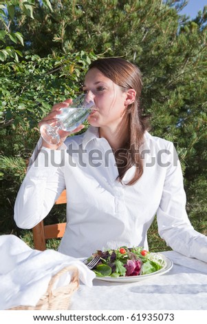 Young woman drinking water and eating a healthy salad outdoors on a restaurant patio