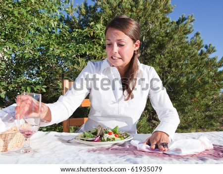 Embarrassed young woman trying to clean after spilling wine on white table cloth