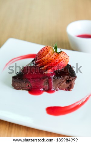Chocolate Cake topping with sliced strawberry and raspberry sauce placed  on white square dish