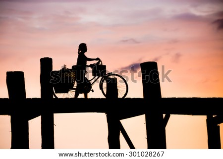 Silhouetted person with a bike on U Bein Bridge at sunset, Mandalay Myanmar