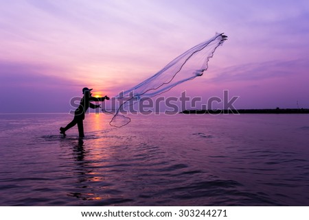 Silhouette of fisherman throwing net at sunset.
