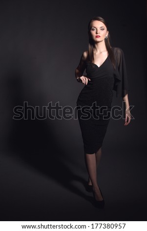 Young beautiful woman in elegant black dress dark studio background