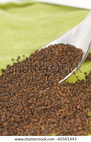 Loose black tea leaves spill from a spoon onto green linen
