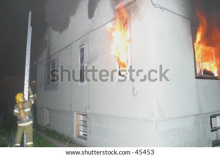 a firefighter carries a ladder to the side of a house on fire