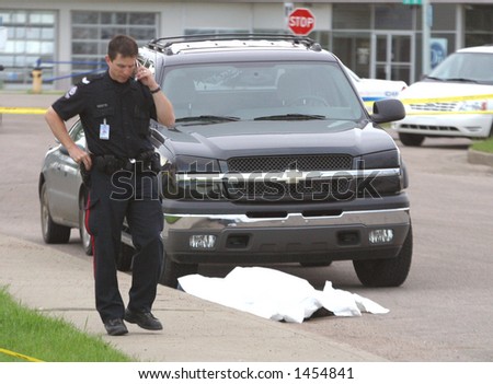 A policeman makes a cell call while standing beside a shooting victim.