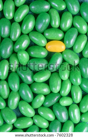 A single yellow jelly bean with a group of green jelly beans.