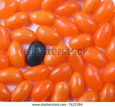 A single black jelly bean with a large number of orange jelly beans.