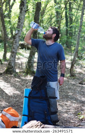 Hiker drinking water in forest at rest, backpack standing on the ground