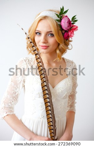 Beautiful bride with flowers in her hair posing over white with long feather, fine art style