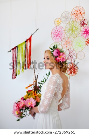 Beautiful blonde bride with bright multicolored bouquet and flowers in her hair, half-turn, bare back