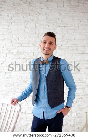 young business man standing by chair with serious expression on a background of white brick wall