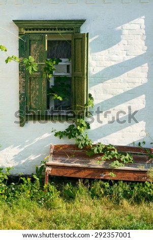 grunge white wall with green window with shutters, shadows, wild grape leaves and bench