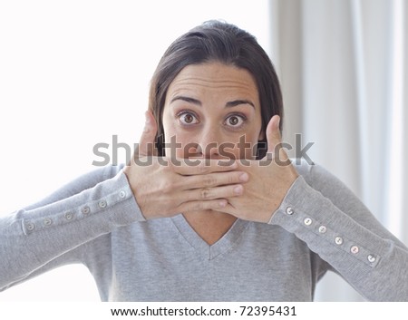 Closeup portrait of young woman covering her mouth with both hands